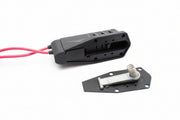 Two black plastic components with pink wires on a beige surface